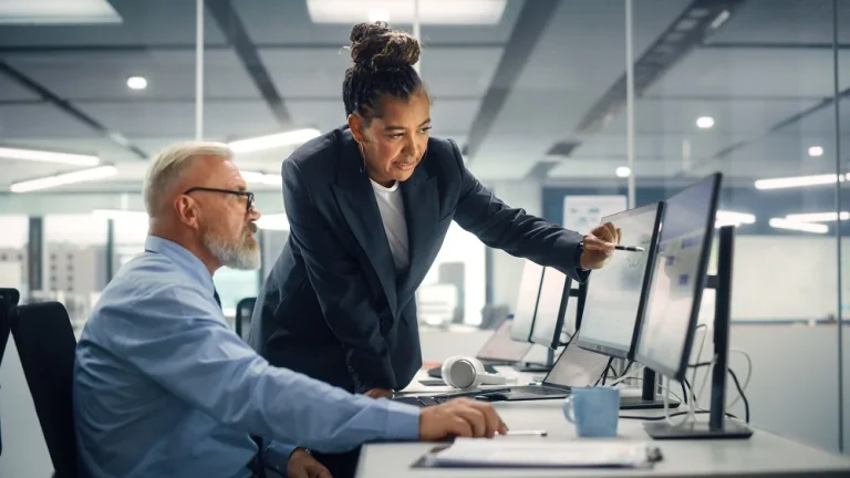 Two colleagues reviewing data together at a multi-monitor workstation